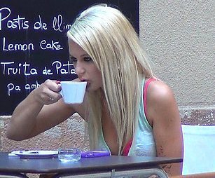 A pretty long haired blonde is drinking coffee in a coffee shop.