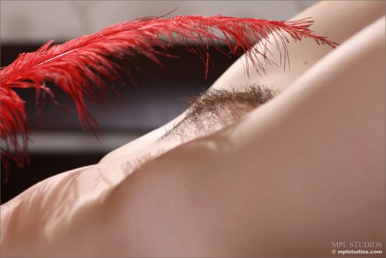 Eugenia holds a long red feather over her pubic hair.